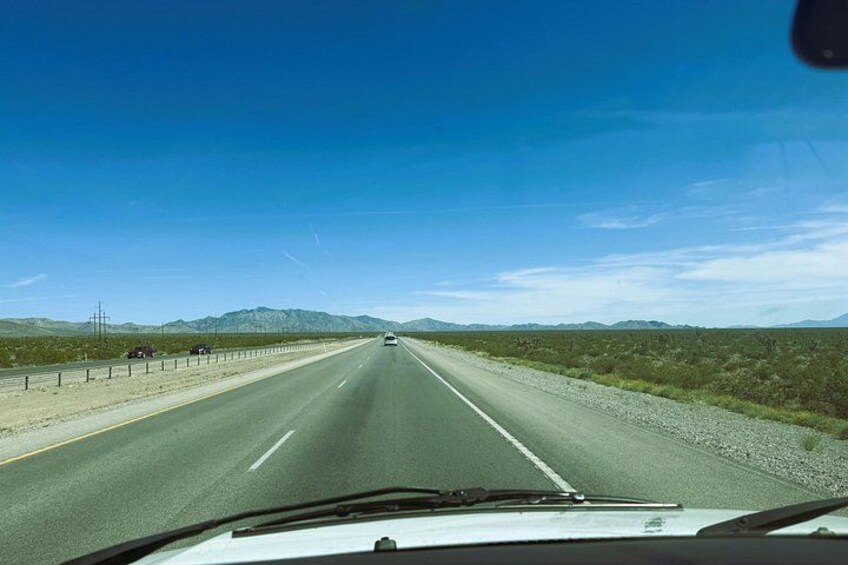 Una autopista bajo un cielo azul despejado, montañas distantes y vegetación escasa. 5