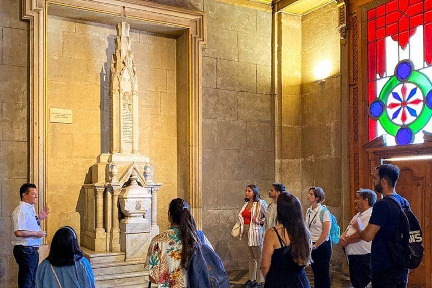 Eine Gruppe von Personen betrachtet ein Steins Denkmal in einem Gebäude mit einem Buntglasfenster. 3