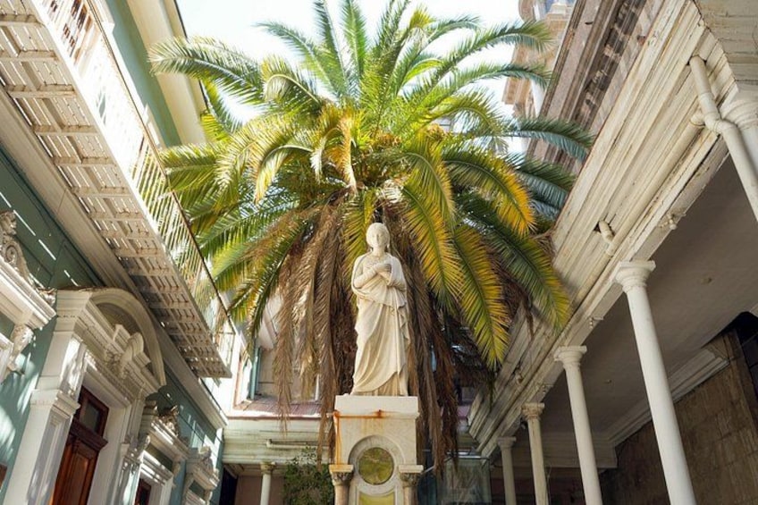 A statue in a covered courtyard with columns and a palm tree. 5