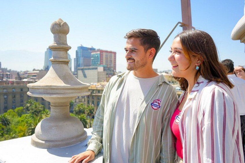 A couple standing on a balcony with a cityscape in the background. 2