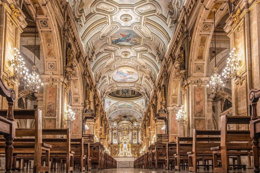 An ornate church interior with high ceilings, detailed frescoes, and rows of wooden pews. 4