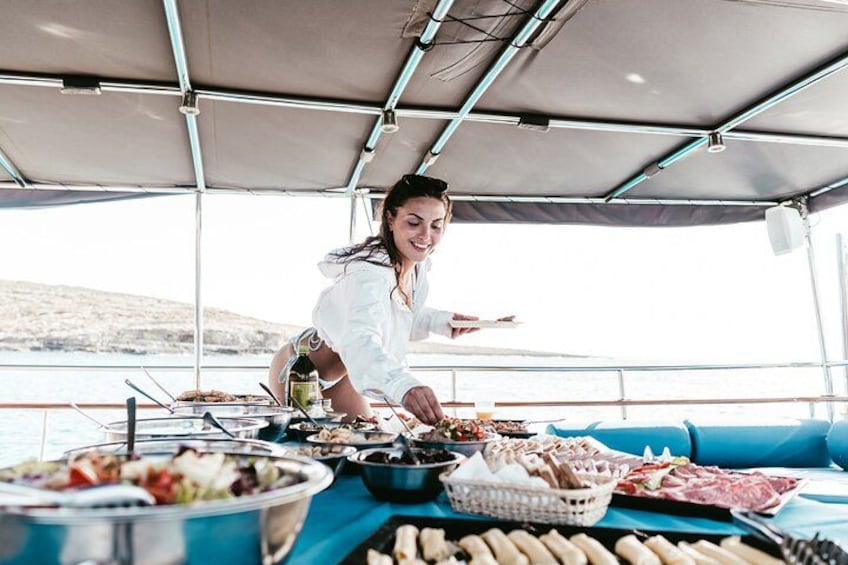 Eine Person serviert Essen auf einem Boot, mit einem Tisch voller Speisen und einer malerischen Wasserlandschaft im Hintergrund. 5