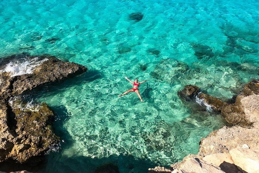 Eine Person treibt in klarem, türkisblauem Wasser, umgeben von Felsformationen. 3