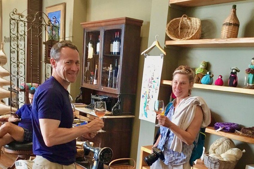 A person holding a glass of wine, another person in the background, and a room with shelves and a cabinet. 2