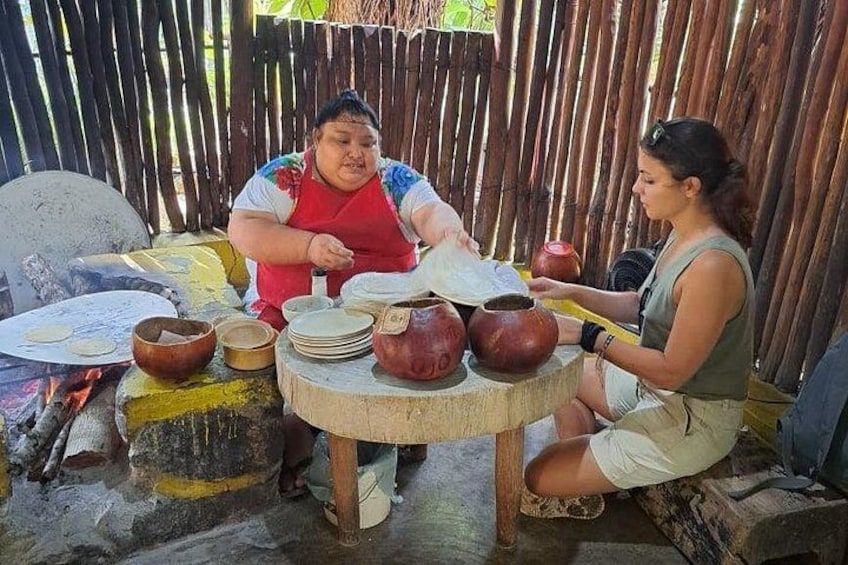 Dos personas cocinando al aire libre con ollas de barro y una mesa de madera. 3