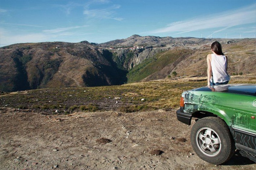 A person sitting on a green vehicle, overlooking a mountainous landscape with a clear sky. 1