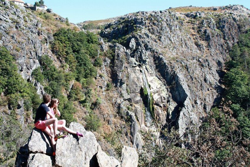 Two people sitting on a rock ledge overlooking a rocky cliff with sparse vegetation. 2