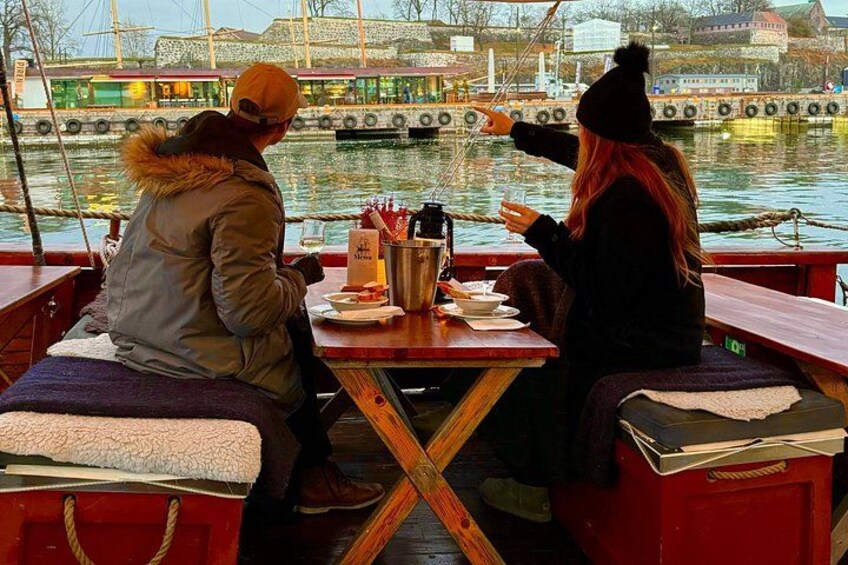 Twee personen zitten aan een tafel op een boot, met een stadsbeeld op de achtergrond. 5