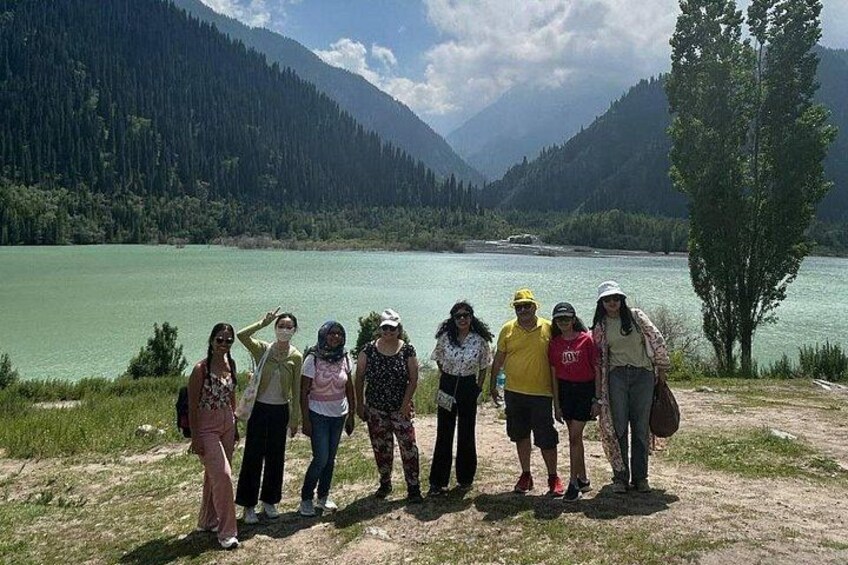 Un grupo de personas de pie junto a un lago, con montañas al fondo. 4