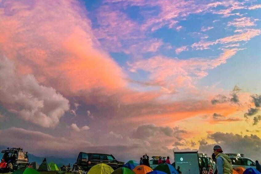 A sunset with colorful clouds, tents, and vehicles at a campsite. 2