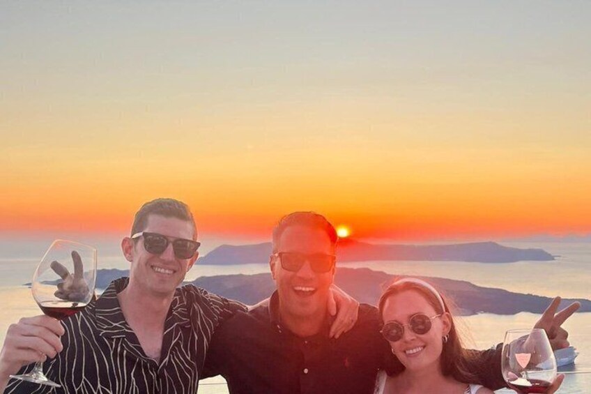 Tre persone brindano con calici di vino sullo sfondo di un tramonto. 3
