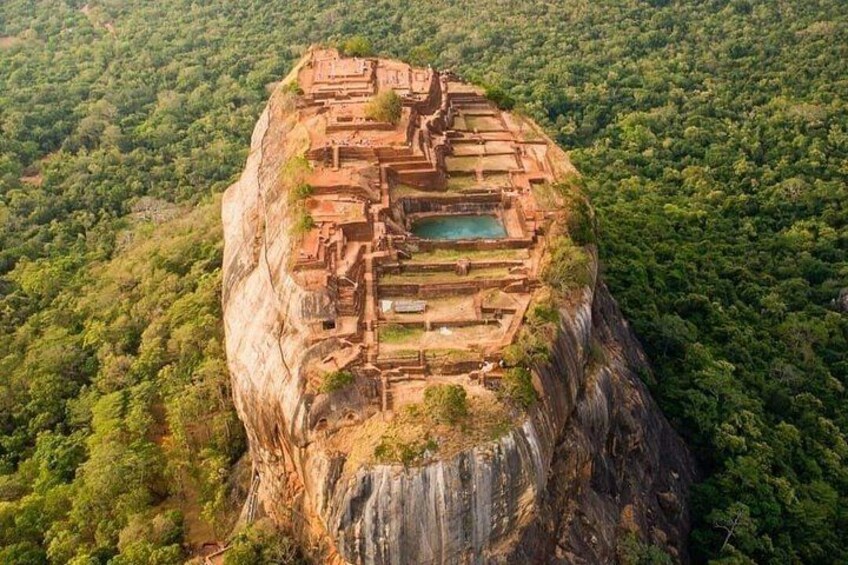 An ancient cliffside city with ruins and a pool. 1
