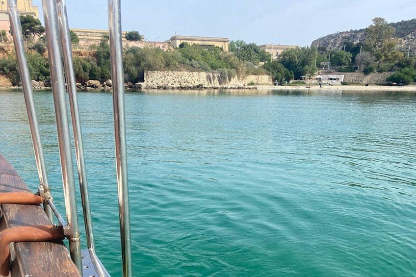 A calm body of water with a wooden boat in the foreground, a rocky shoreline, and buildings in the background. 2