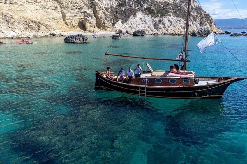 A boat with people on a clear blue sea, rocky cliffs in the background. 1