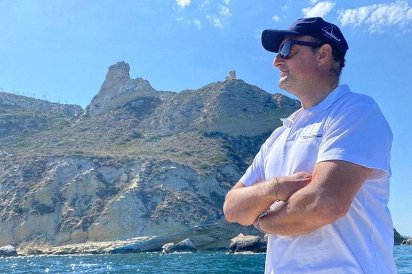 A person standing on a boat with a rocky coastline and a prominent rock formation in the background. 4