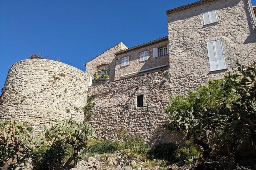 A stone building with a round tower, a small window, and a balcony with plants. 2