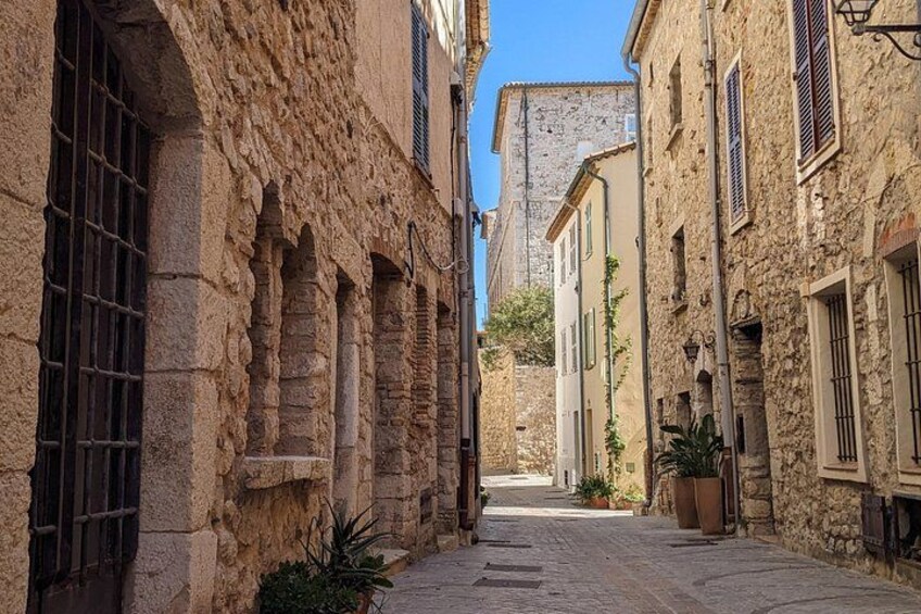 A narrow cobblestone street flanked by old stone buildings with arched windows and shutters. 5