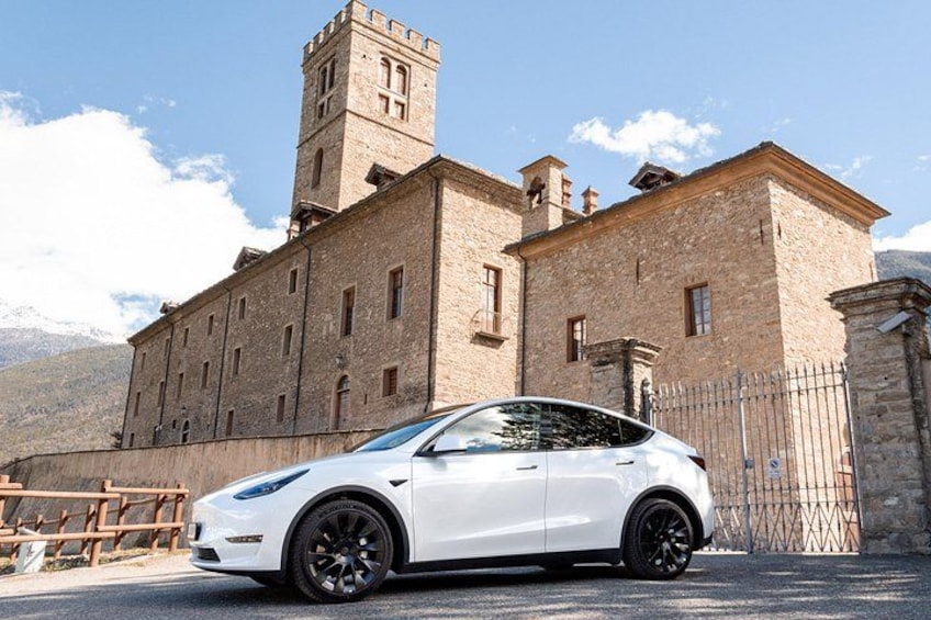 A white car parked in front of a historic building with a tower. 1