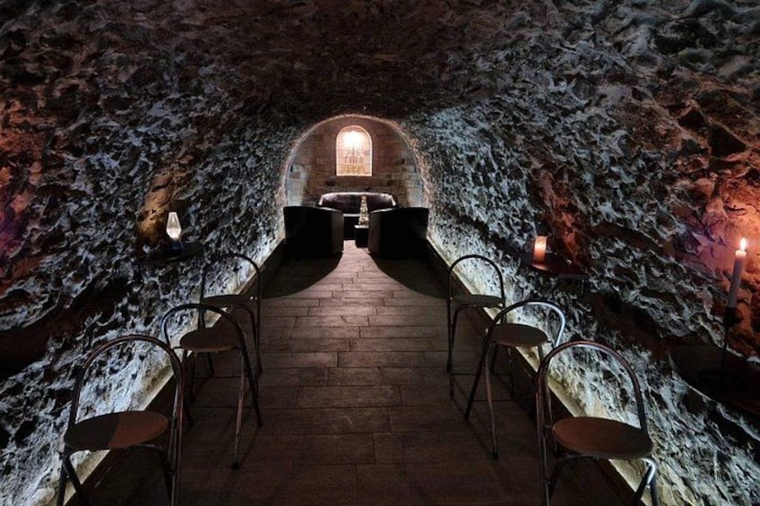 An underground dining area with stone walls, a wooden floor, and candle-lit tables. 2