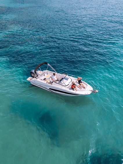 A white motorboat with two people on board, floating on turquoise water. 1