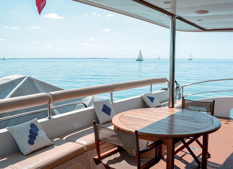 A boat deck with a round wooden table, cushioned seating, and a view of the sea with sailboats. 5