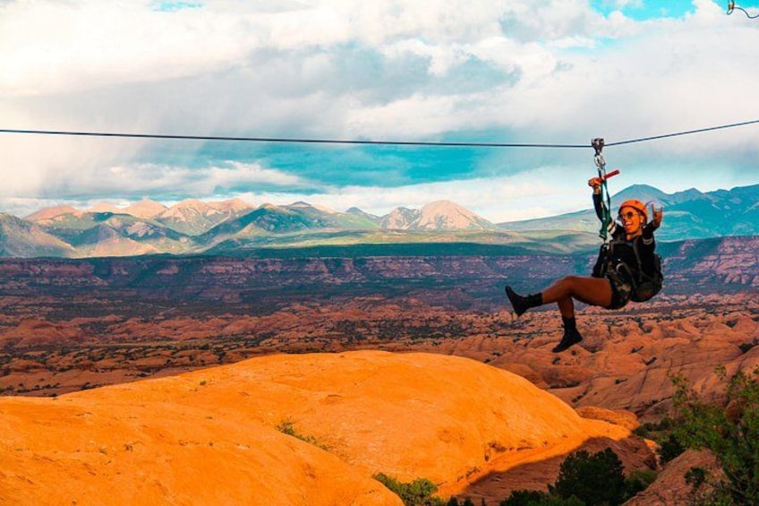 A person zip-lining over a desert landscape with mountains in the background. 1