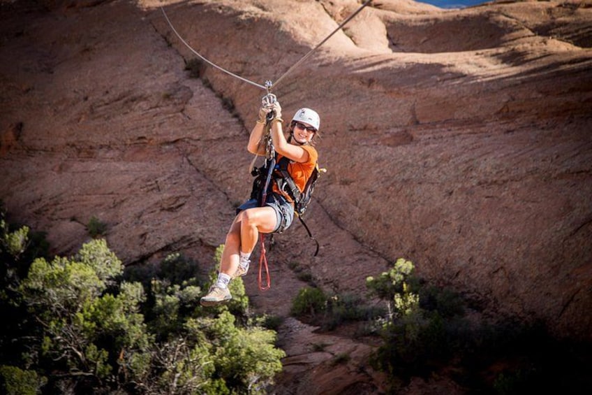 A person zip-lining through a canyon with rocky cliffs and sparse vegetation. 4