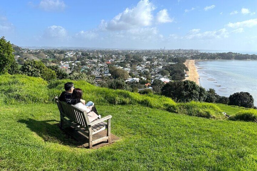 A couple sitting on a bench overlooking a coastal town with a beach. 2