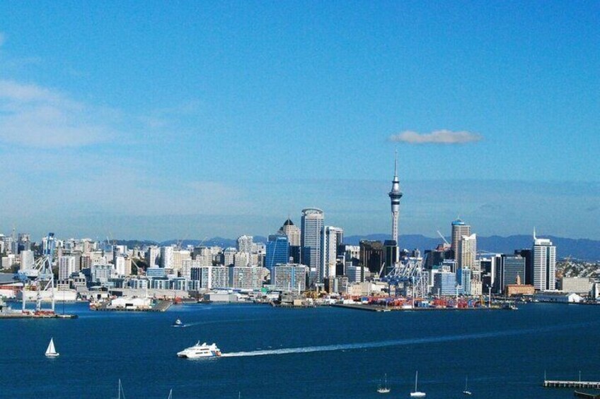 A city skyline with a prominent tower, a body of water with boats, and a clear sky. 1