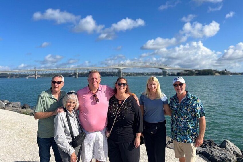 A group of people standing by a waterfront with a bridge in the background. 5