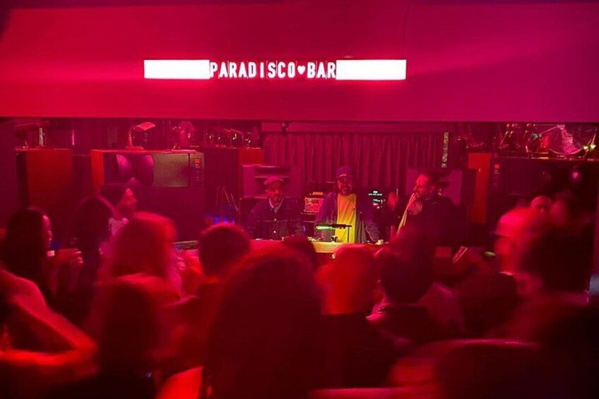 L’intérieur d’un club avec une cabine de DJ, un éclairage rouge et une foule de personnes. 2