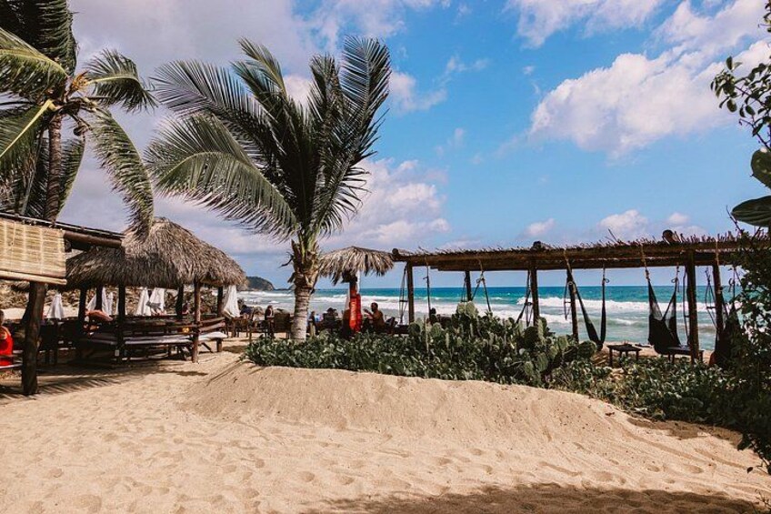 Een strand met palmbomen, een constructie met rieten dak en een schommel. 1