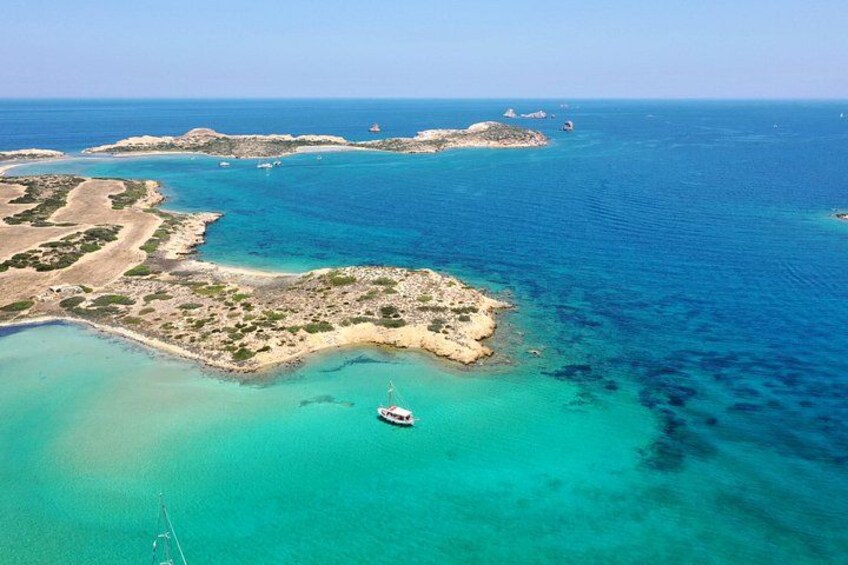 An aerial view of a coastal area with clear turquoise waters, a small island with rocky terrain, and a boat anchored near the shore. 4