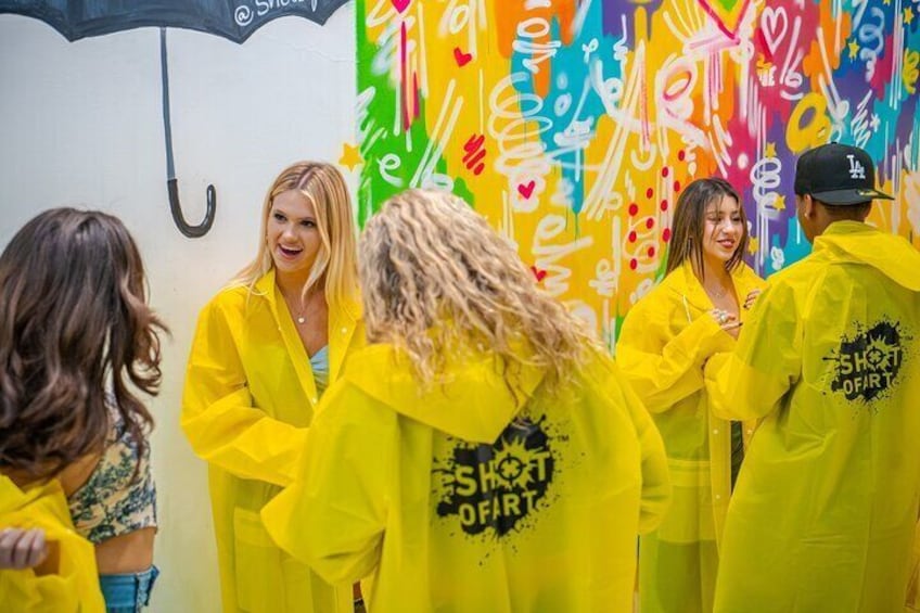Un groupe de personnes, vêtues de ponchos de pluie jaunes, se tient devant un mur recouvert de graffitis colorés. 2
