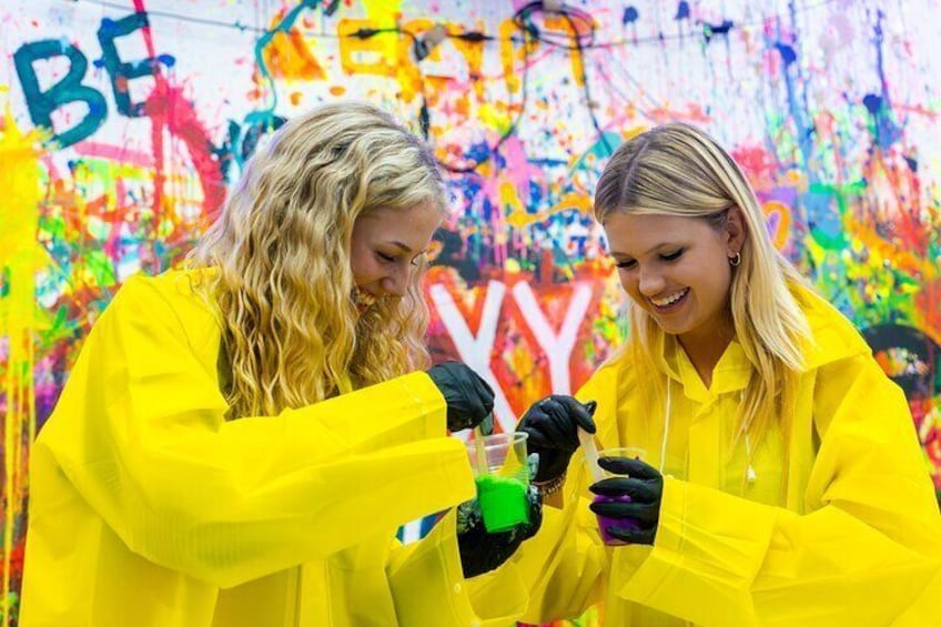 Dos personas con abrigos amarillos realizando un experimento con un líquido verde en un matraz. 4