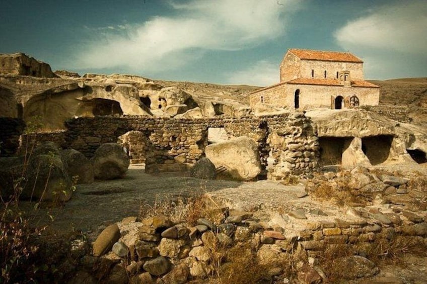 Ancient ruins with stone structures and a small building with a red roof. 2