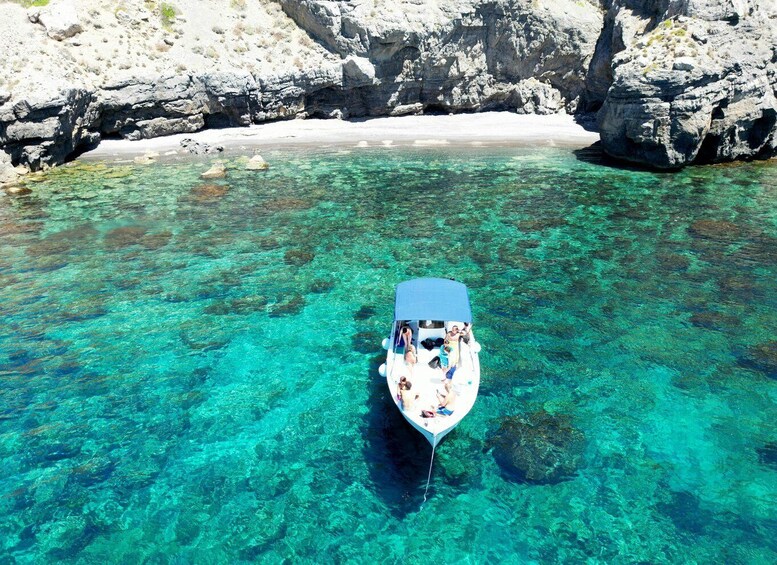 A boat anchored in clear turquoise water with rocky cliffs in the background. 1