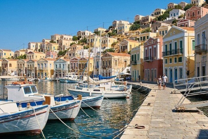 A harbor with boats docked, a stone walkway, and colorful buildings on a hillside. 1