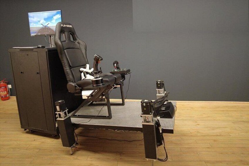 Una silla gamer con un volante y pedales montados, un monitor y una caja de control. 2