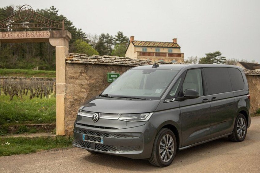 A gray Volkswagen van parked in front of a stone wall with a sign that reads 'LOS DES ISSAIRS.' 2