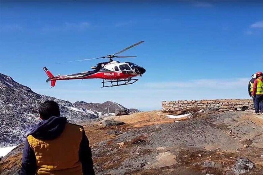 A helicopter flying over a rocky terrain with a person standing on the ground. 2