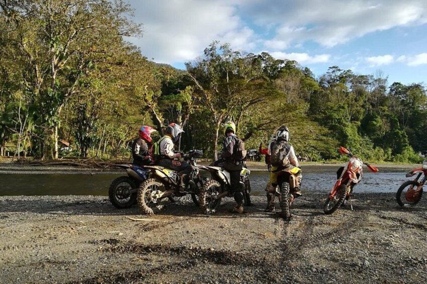 Un groupe de personnes sur des motos tout-terrain, près d’une rivière, entourées d’arbres et de collines. 5