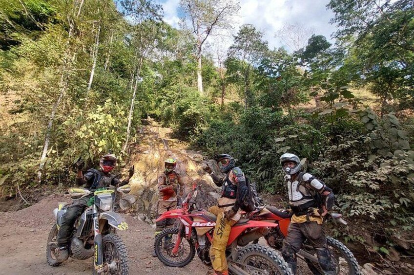 Quatre motos tout-terrain sont garées sur un chemin de terre, entourées d’arbres. 2