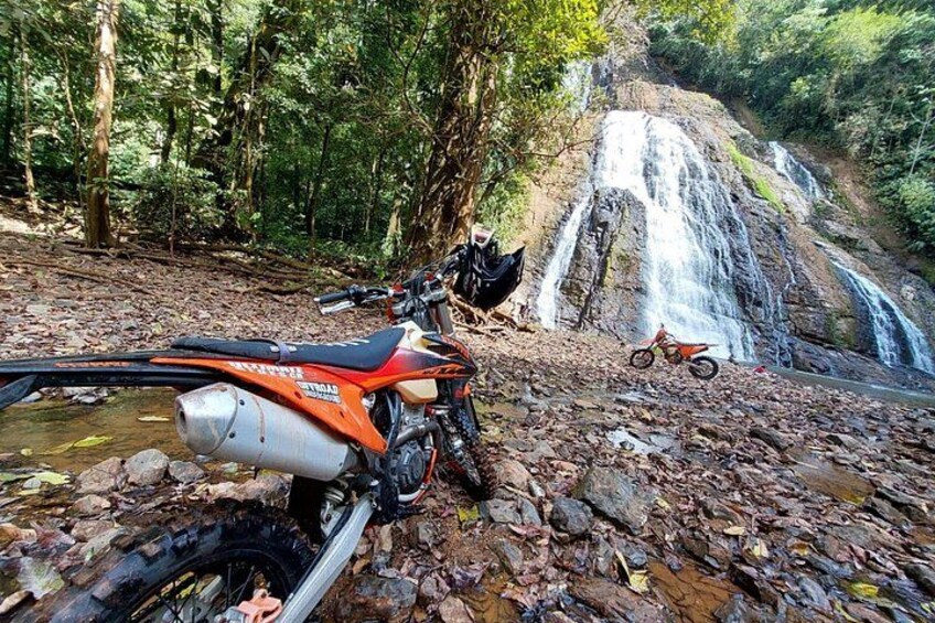 Une moto tout-terrain est garée près d’une cascade, dans une zone boisée. 1