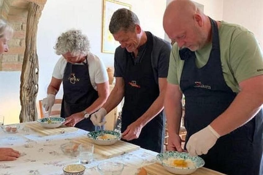 Three people wearing aprons, preparing food at a table with bowls and utensils. 1