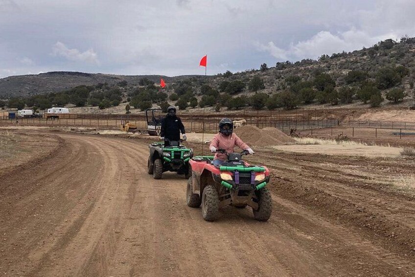 Two people riding ATVs on a dirt road with a flag in the background. 5