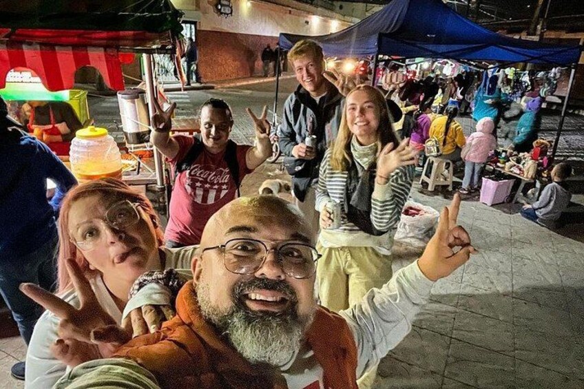 Un groupe de personnes se trouve sur un marché en plein air, où l’on peut voir des tentes et des étals de nourriture. 1