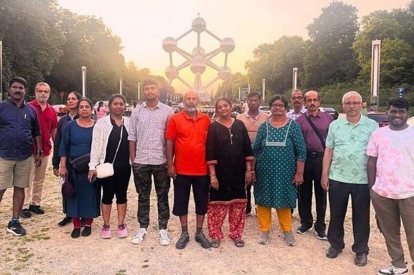 A group of people standing outdoors with a large structure in the background. 1