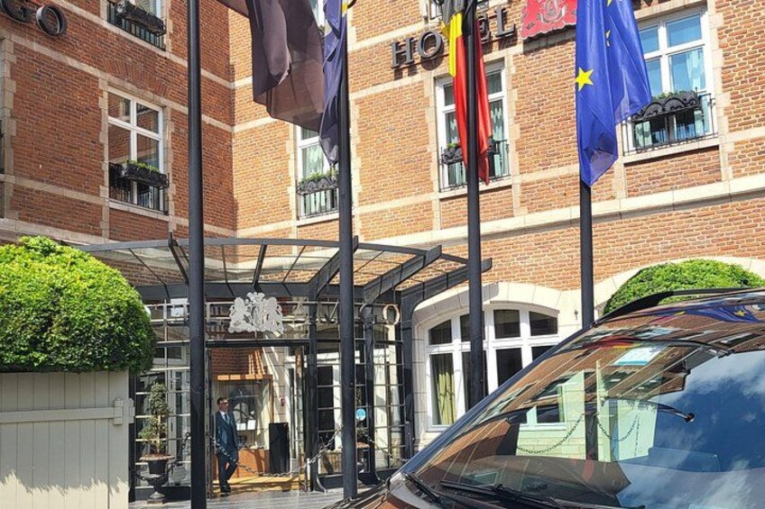 A hotel entrance with a glass canopy, flags, and a car parked in front. 4