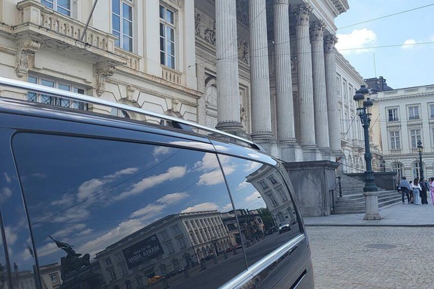 A black van parked on a cobblestone street in front of a classical building with columns. 2